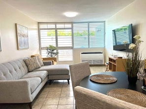 Een woonkamer met een modulaire bank, een eettafel met placemats, een flatscreen televisie en een potplant.