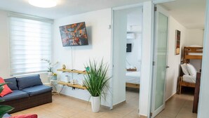 Una sala de estar con un sofá, una mesa de centro, una planta y un cuadro en la pared.