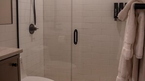 Ein Badezimmer mit gefliesten Duschwänden, Toilette, Handtuchhalter und Seifenspender.