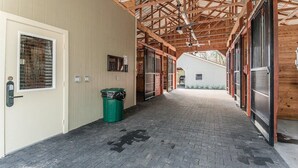 A covered walkway with a brick floor, wooden beams, and a trash bin. - Superior Queen Two-Bedroom Cottage (Bronson)