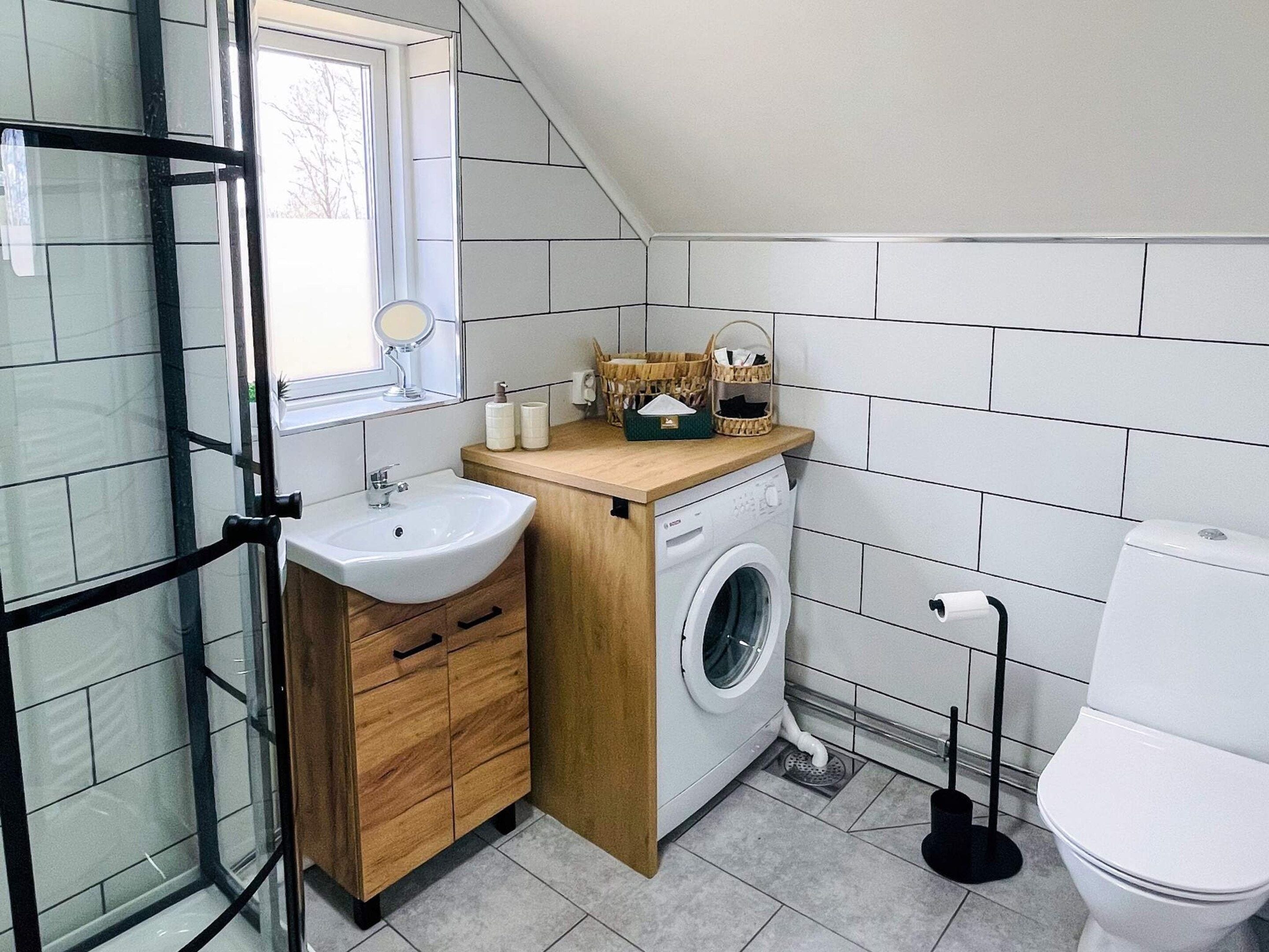 A compact bathroom with a sink, mirror, washing machine, and toilet.