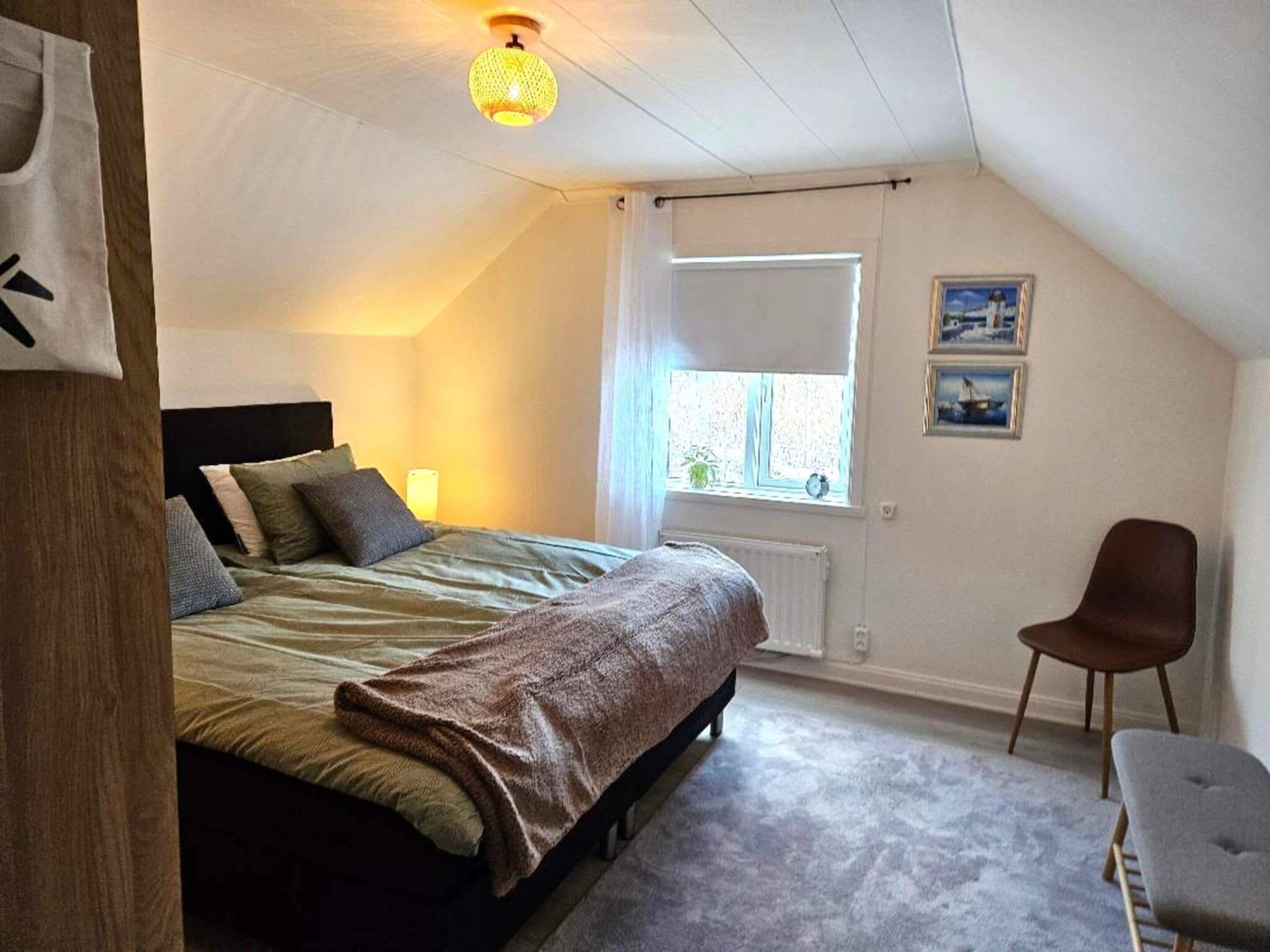 Un dormitorio con cama, ventana, silla y radiador.