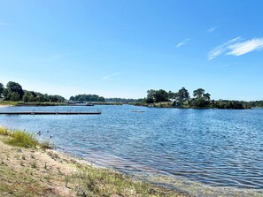 Un llac tranquil amb un moll, cel serè i arbres al fons.