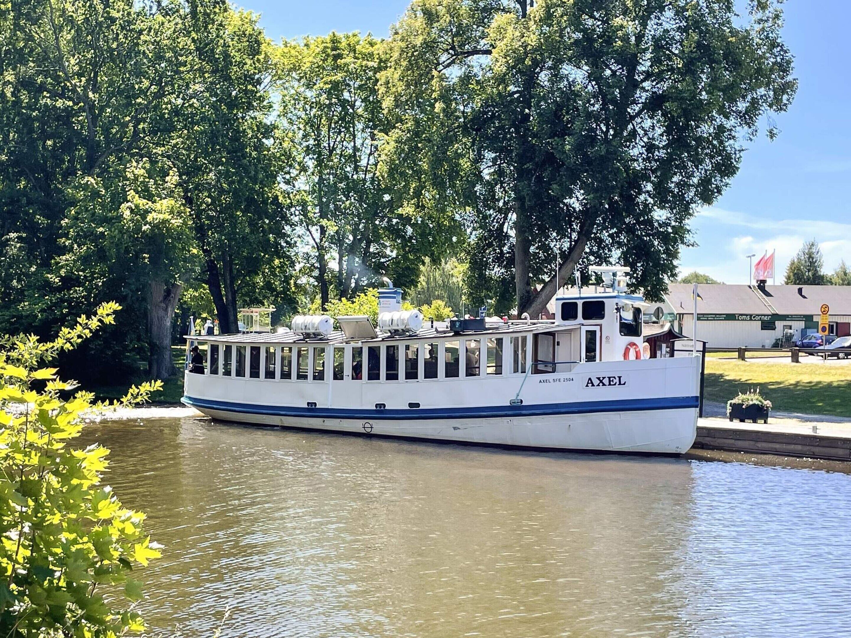 Un barco de paseo atracado en un muelle, con un edificio que dice 'Toms Corner' al fondo.