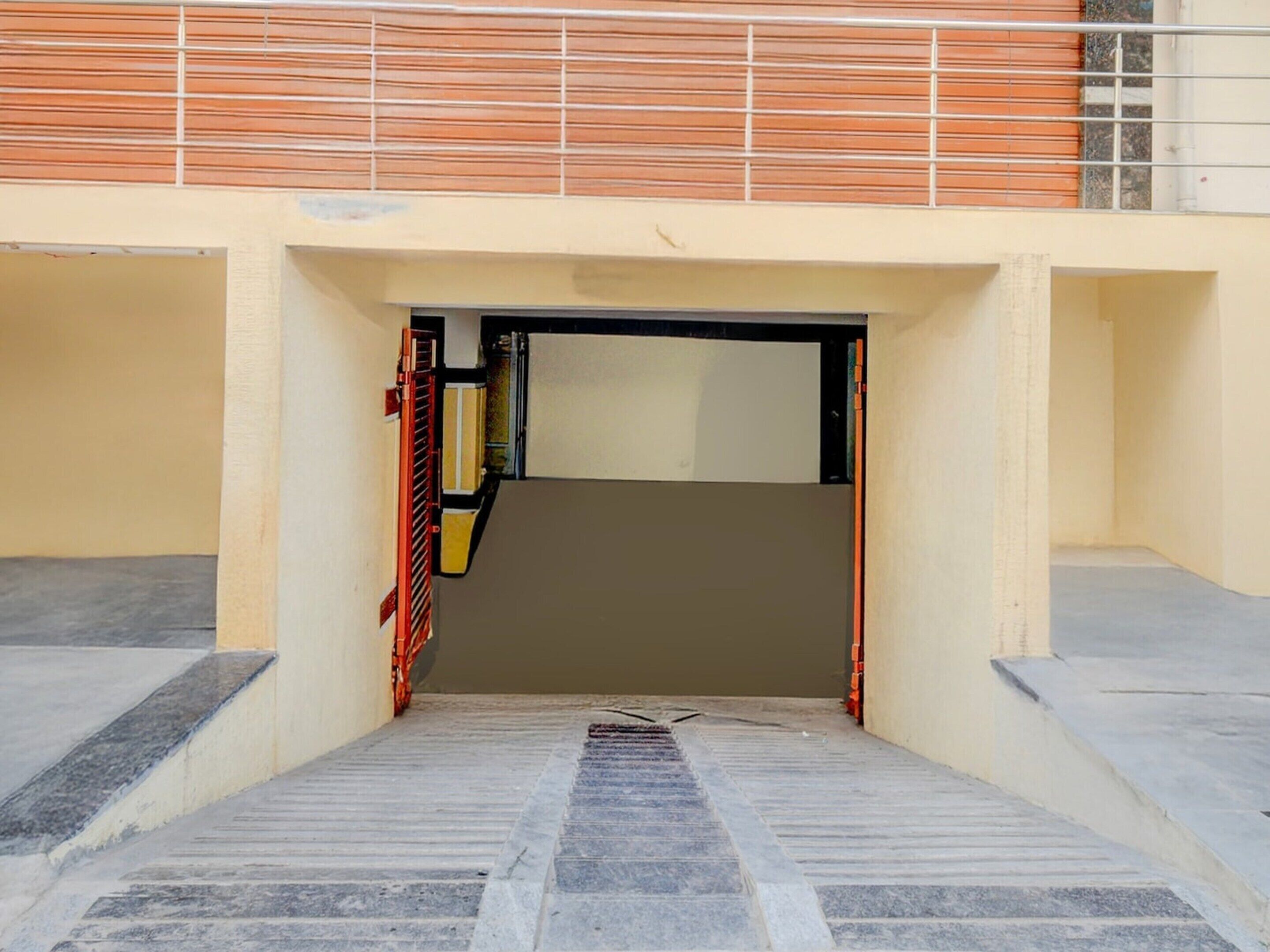 A building entrance with a ramp leading up to a door, surrounded by a beige wall and a metal railing.