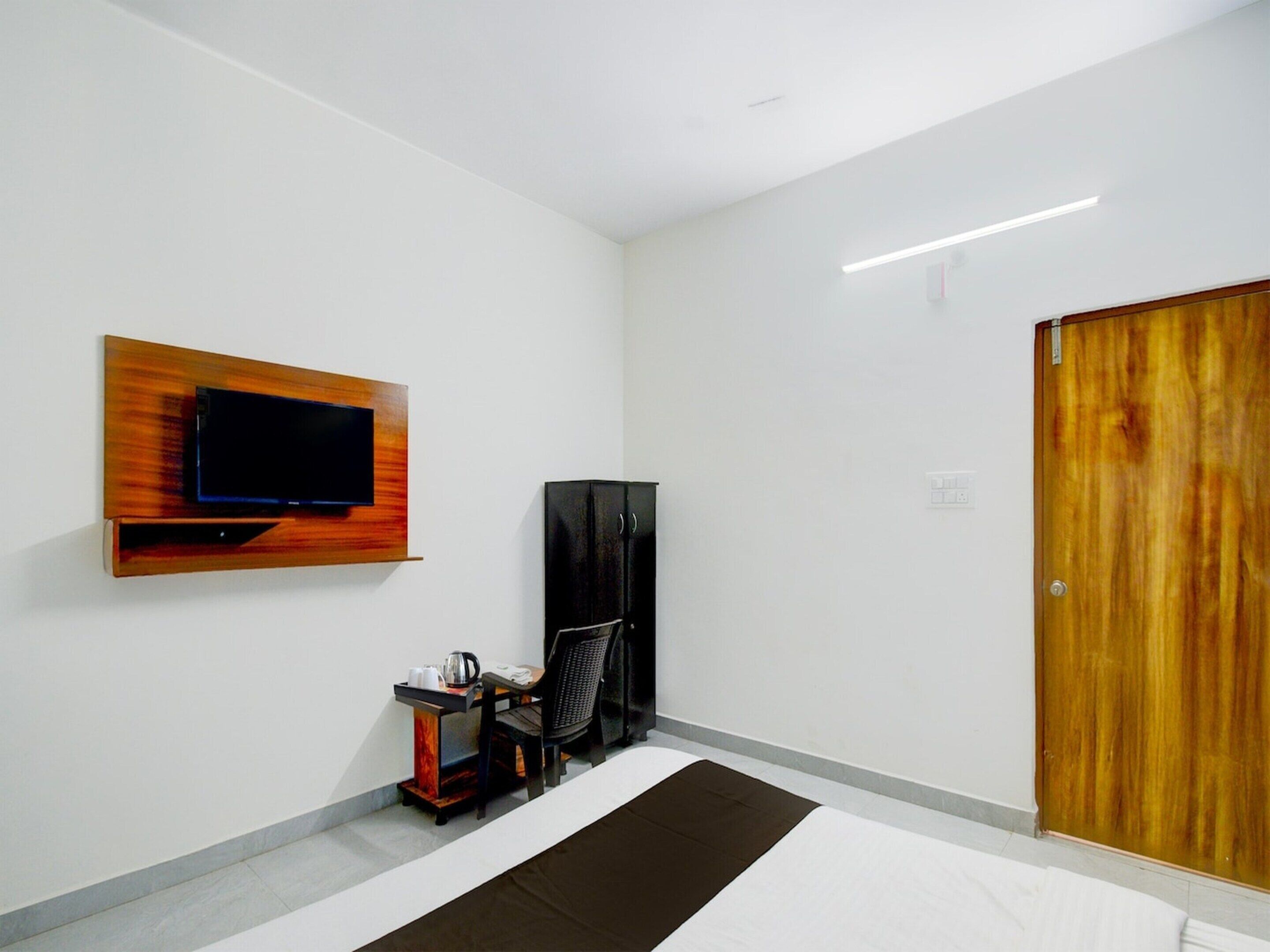 A hotel room with a flat-screen TV mounted on the wall, a wooden wardrobe, a small table with a kettle, and a bed with a brown and white striped bedspread.