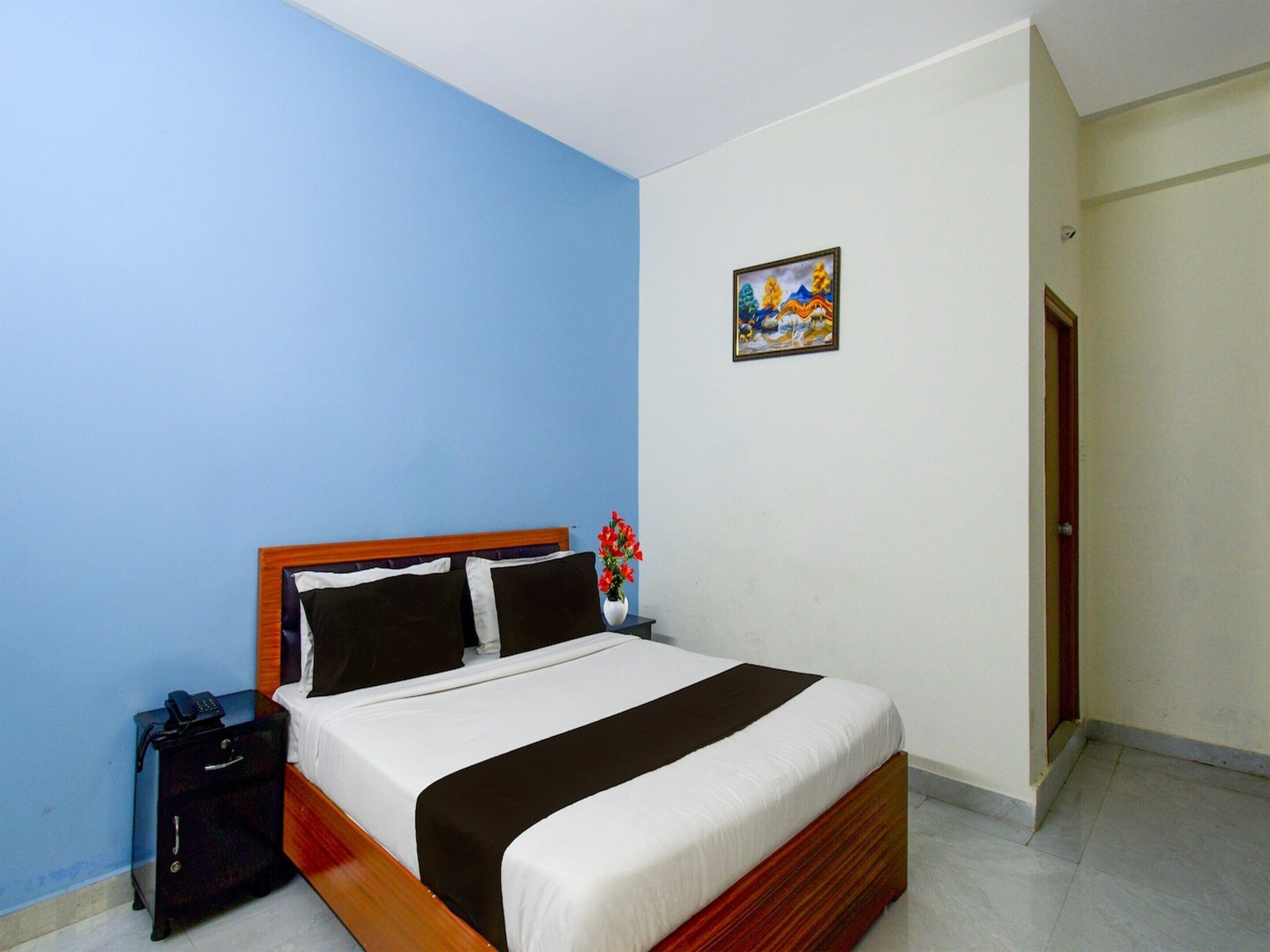 A bedroom with a bed, a nightstand, a telephone, a vase with flowers, and a painting on the wall.