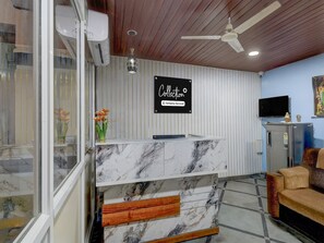 Una reception con piano in marmo, una ventola a soffitto, un televisore a parete e un cartello con la scritta 'Collection Company-Serviced'.