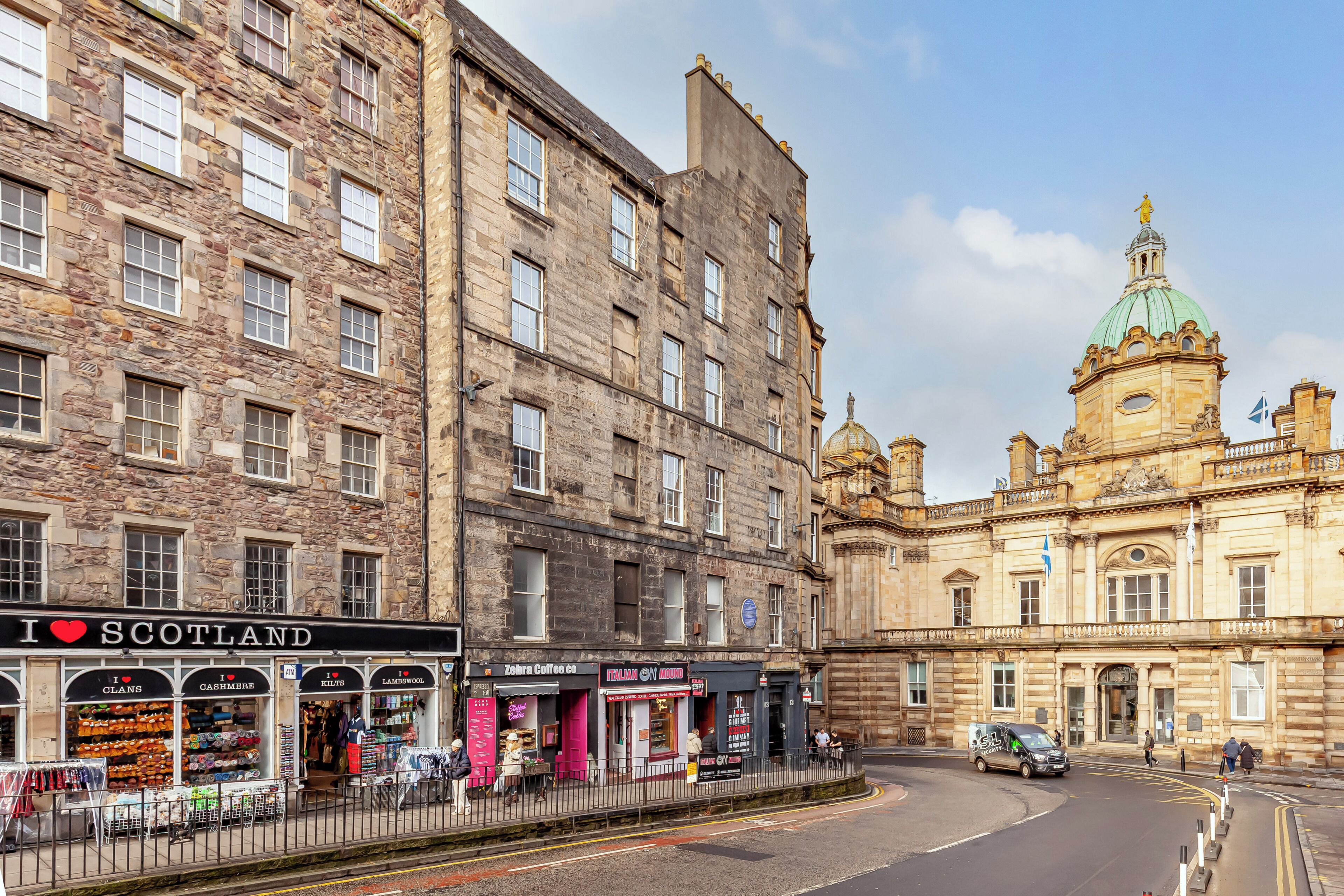 A historic stone building with shops on the ground floor, including a coffee shop and a store named 'Zebra Coffee Co.'