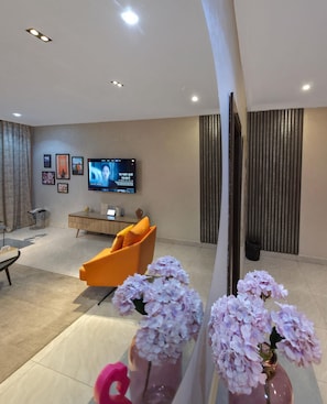 A modern living room with a flat-screen TV, a sofa, a coffee table, and decorative vases. - Noble Lite Suites   (Abuja)