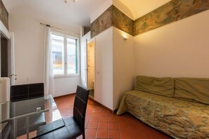 Ein Zimmer mit Glastisch, schwarzem Stuhl, einer Couch, einer Tür und einem Fenster.