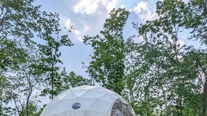 A geodesic dome structure with a wooden deck, outdoor seating, and a gravel ground.