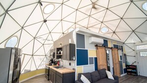 A geodesic dome interior with a kitchen, seating area, and a sliding door.