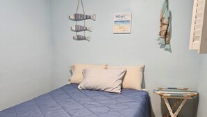 A bedroom with a bed, pillows, a wall-mounted fish decoration, a small table, and a framed picture.