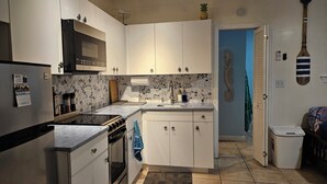 A compact kitchen with white cabinets, a microwave, a stove, and a sink.