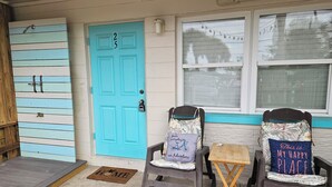 A porch with a blue door, two rocking chairs, a small table, and a window with blinds.