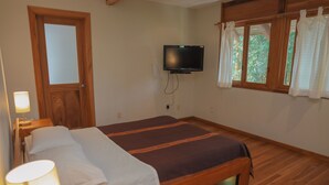 Una habitación con cama, televisión montada en la pared, ventana con cortinas y una puerta.