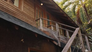 Un edificio de madera con un balcón, una ventana y una palmera al fondo.