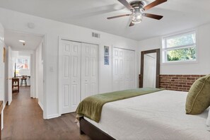 Ein Schlafzimmer mit Bett, Deckenventilator, Fenster und einer Tür zu einem weiteren Raum.