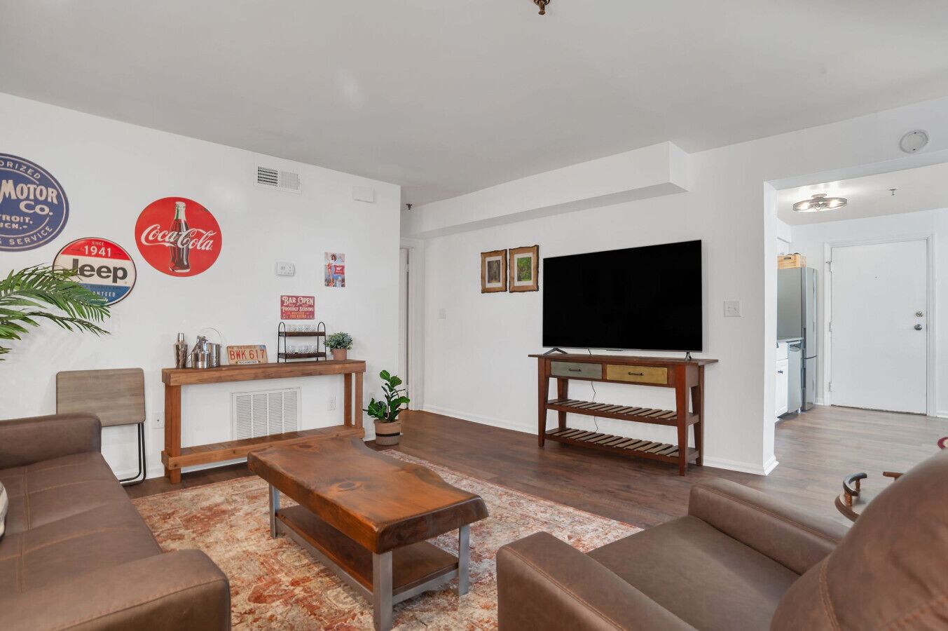 Un salón con sofá, mesa de centro, televisor y una pared decorada con logotipos de autos antiguos.