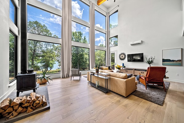 Ein geräumiges Wohnzimmer mit großem Fenster, Kamin, Sofa, Couchtisch und Fernseher an der Wand.