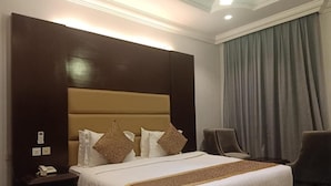 A hotel room with a large bed, a nightstand with a phone, a chair, and a window with curtains. - Ferbion Hotel Abha (Abha)