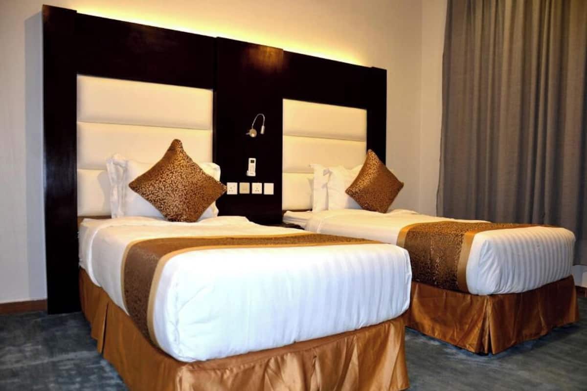 A hotel room with two beds, each with white linens and brown headboards.
