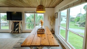 Ein Holzinterieur mit einem großen Fenster, einem Holztisch, einer hängenden Leuchte und einem an der Wand befestigten Fernseher.