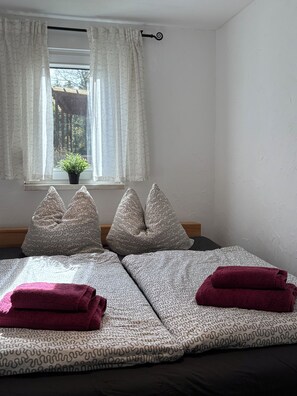 Un dormitorio con cama, almohadas, una ventana con cortinas y una planta en maceta.