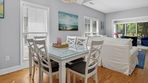 Un coin repas avec une table en verre et des chaises blanches, un salon avec un canapé et un fauteuil bleu, et un lustre.
