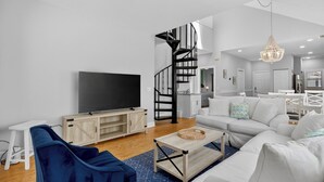 Un salon moderne avec un téléviseur à écran plat, un canapé bleu, un canapé blanc, une table basse en bois et un escalier en colimaçon.