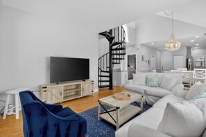 A modern living room with a flat-screen TV, a blue sofa, a white sofa, a wooden coffee table, and a spiral staircase. - Award-Winning Resort Amenities | Links Clubhouse 10 (Isle Of Palms)