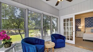 Une pièce dotée de grandes fenêtres, d’un ventilateur de plafond, d’un canapé bleu, d’une petite table ronde et d’un tapis à motifs.