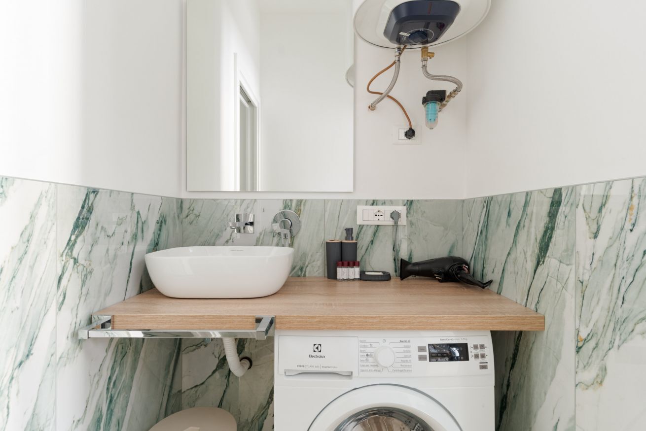 Une salle de bain moderne avec un lavabo blanc, un pare-feu en marbre et un lave-linge.