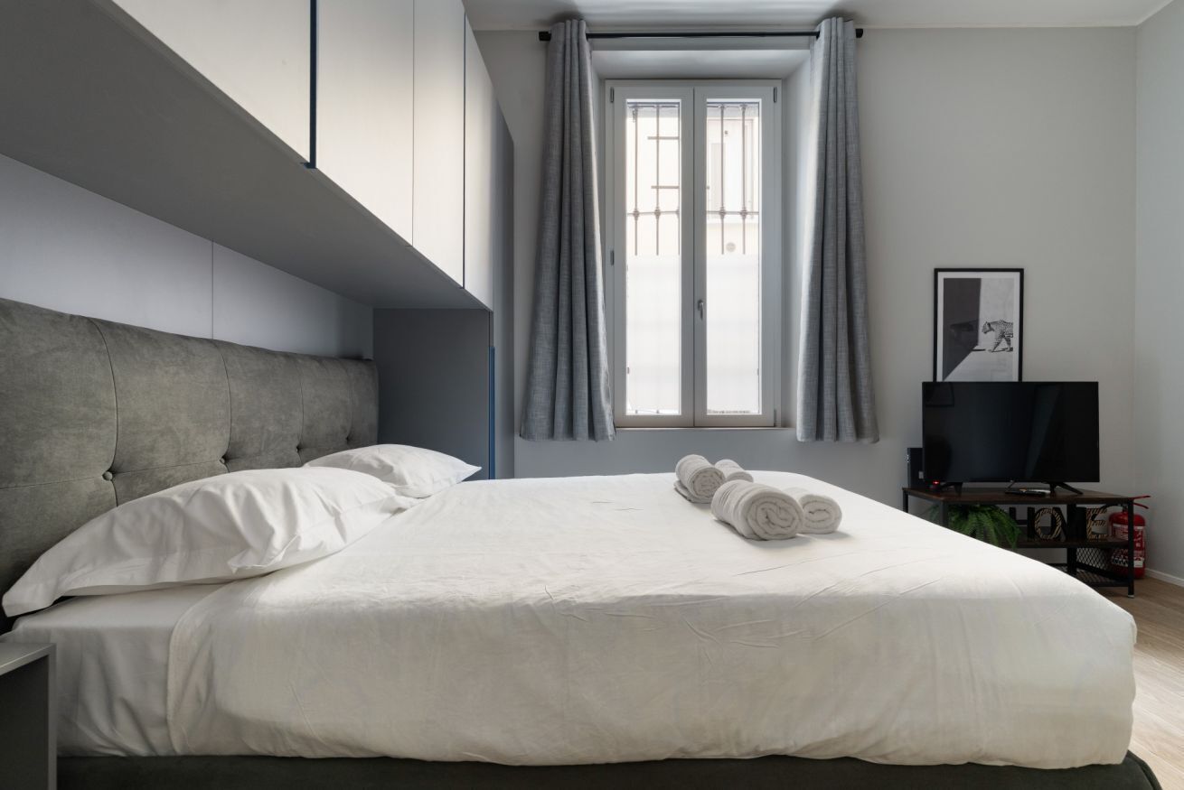 Una camera da letto moderna con un letto grande, una televisione a schermo piatto e una finestra con tende.
