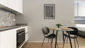 Una cucina moderna con mobili bianchi, un piano di lavoro in granito, forno integrato e zona pranzo con tavolo in vetro e sedie nere.