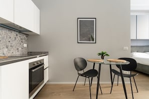 Une cuisine moderne avec des armoires blanches, un comptoir en granit, un four encastré et un coin repas comprenant une table en verre et des chaises noires.