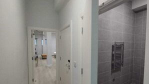 Ein Flur, der zu einem Badezimmer mit einer gefliesten Duschkabine führt.