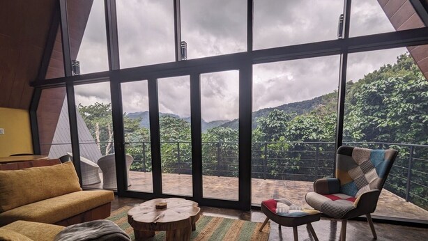 A room with a large window, a sofa, a chair, a small round table, and a book.
