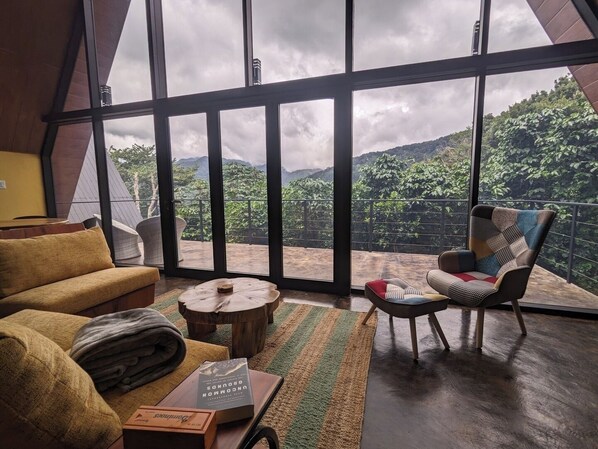 A room with a large window, a sofa, a chair, a small round table, and a book.