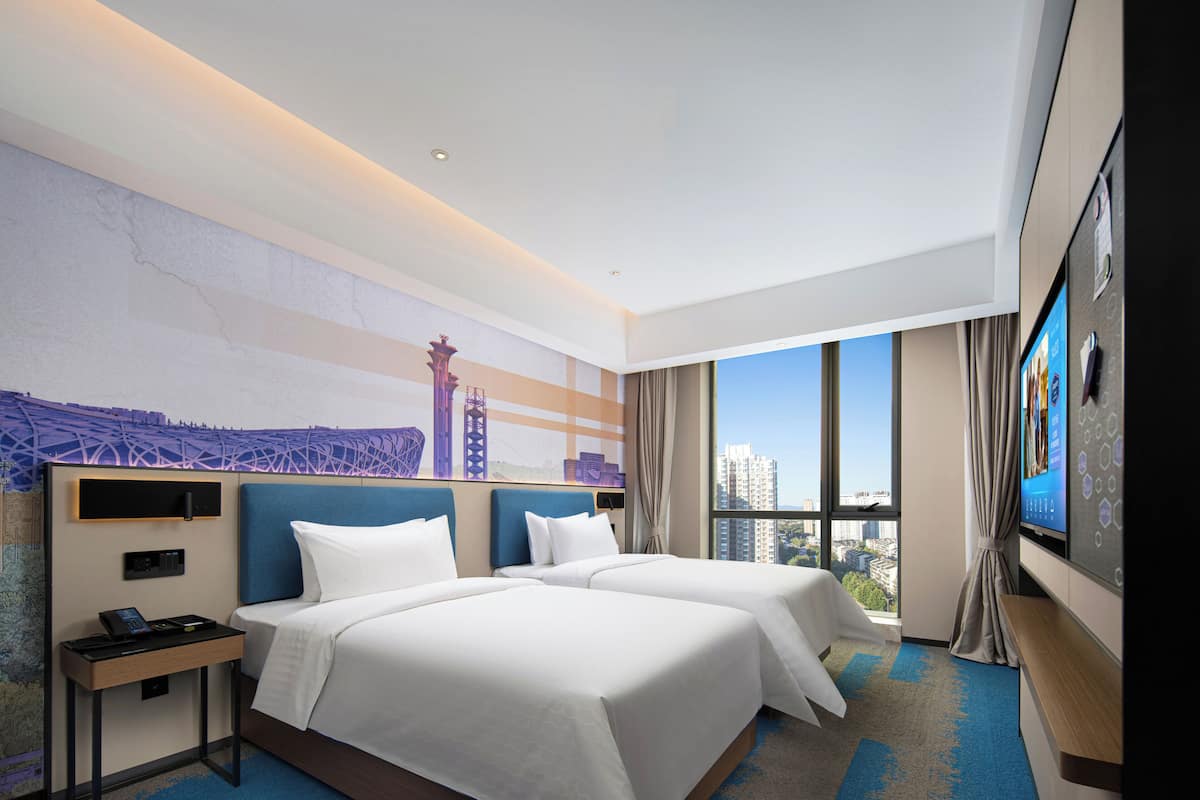 Habitación de hotel con dos camas, un ventanal con vistas a la ciudad, un televisor de pantalla plana y una obra de arte colgada en la pared.
