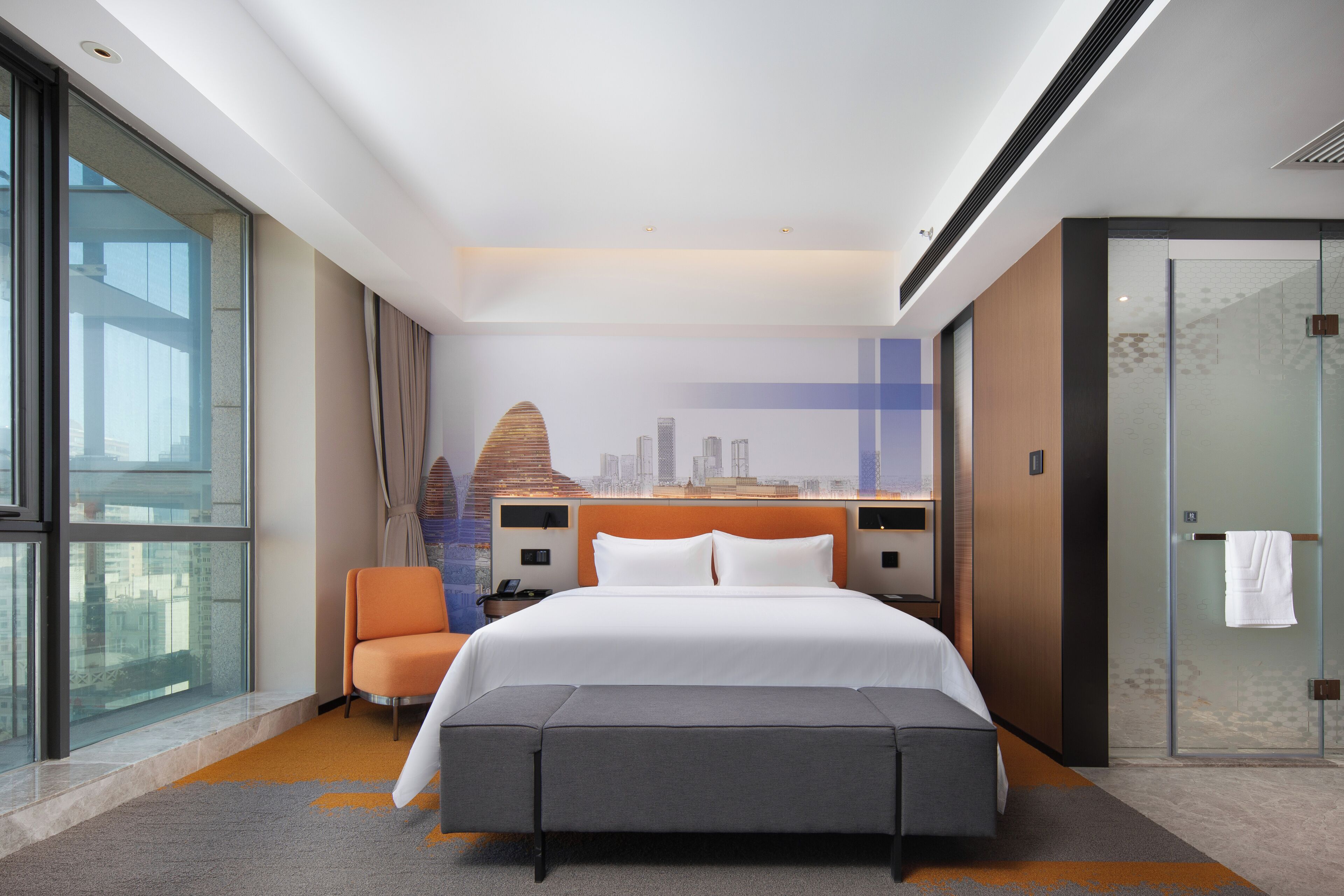 A hotel room with a large bed, a seating area, a glass shower, and a cityscape mural on the wall.