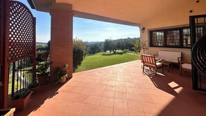 Un patio cubierto con vistas a un paisaje verde, un pilar de ladrillo y mobiliario exterior.