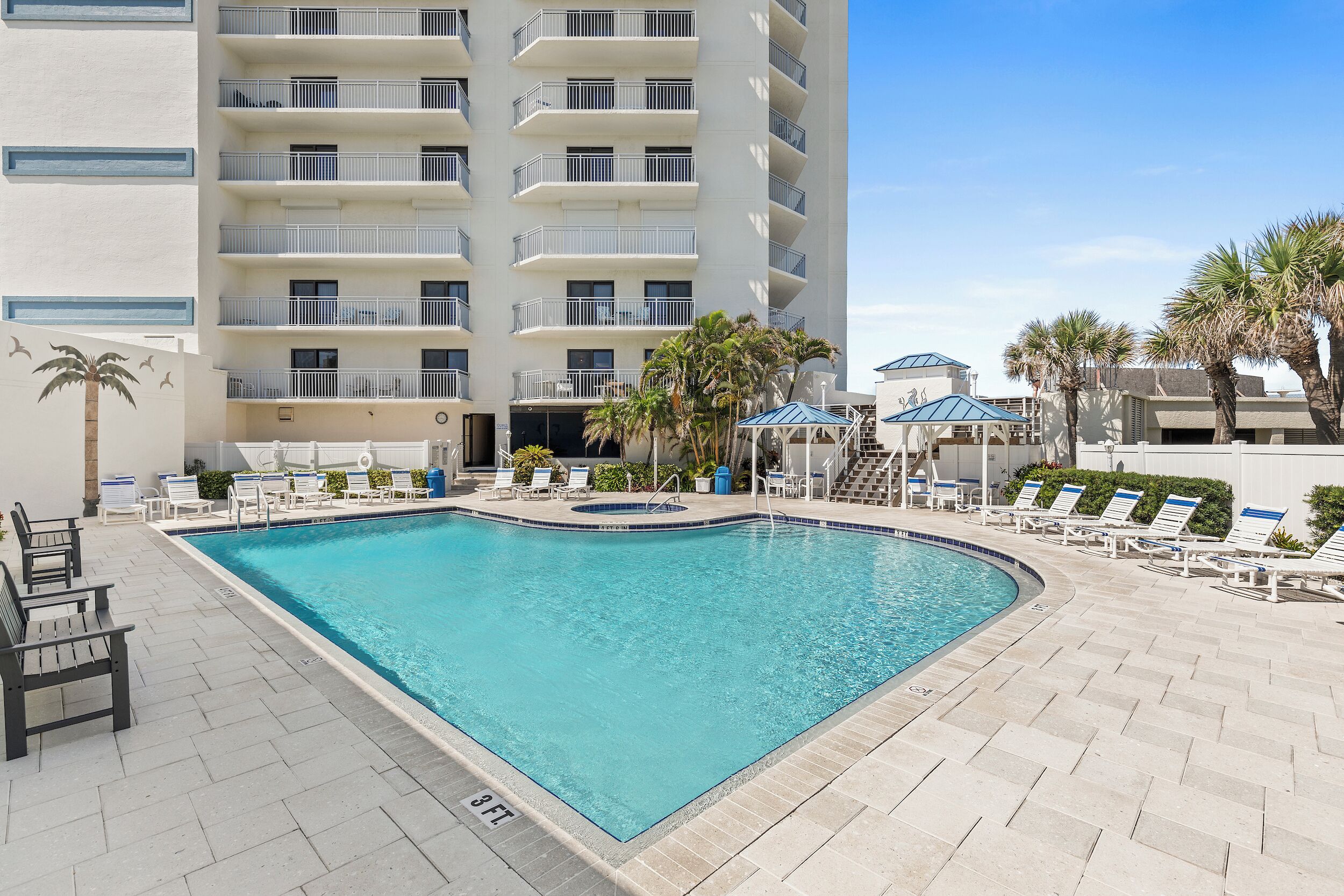 A swimming pool with lounge chairs and a building with balconies.
