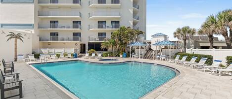 A swimming pool with lounge chairs and a building with balconies.