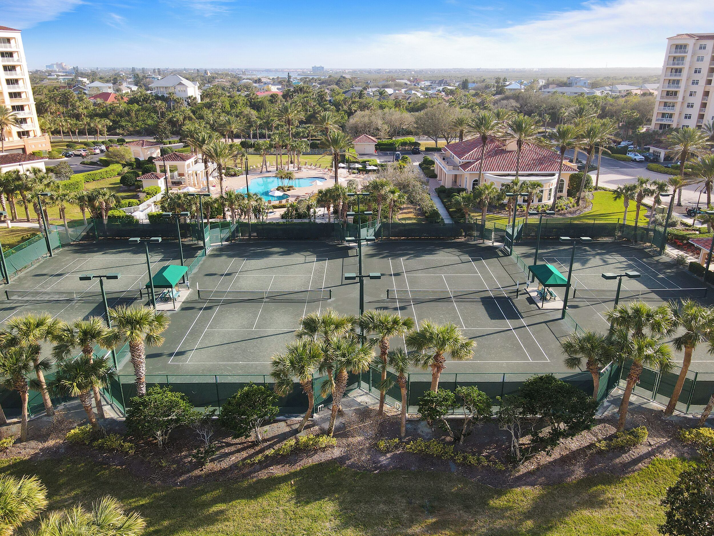 A tennis court surrounded by palm trees and a pool.