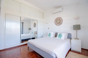 A bedroom with a large bed, a wardrobe, a mirror, a wall-mounted air conditioner, and a bedside lamp. - Casa do Livramento - Fabulous 3 bedroom villa with games room (Carvoeiro)