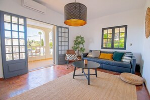 A spacious living area with a sofa, a round table, and a chair. There are large windows and a door leading to an outdoor area. - Casa do Livramento - Fabulous 3 bedroom villa with games room (Carvoeiro)
