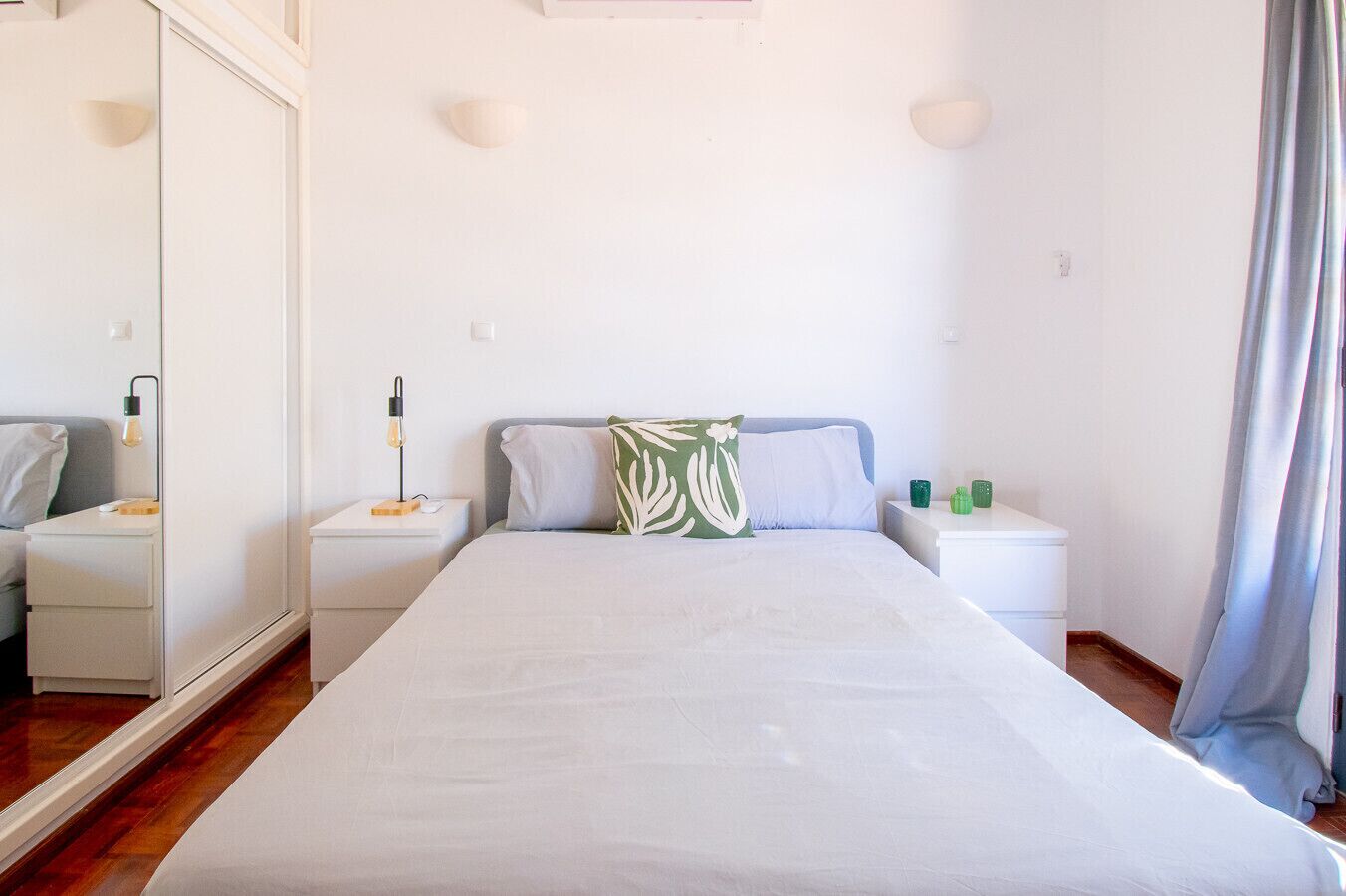 Une chambre à coucher avec un grand lit, deux tables de chevet, un miroir et une petite table de nuit avec une lampe.
