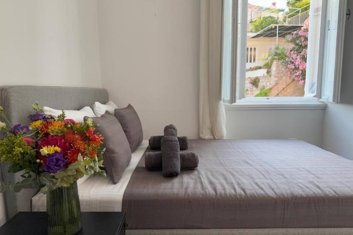 Un dormitorio con cama, almohadas, un jarrón de flores y una ventana con vistas.